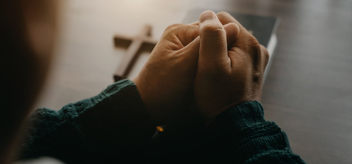 Man praying with a cross and bible on the table in front of him