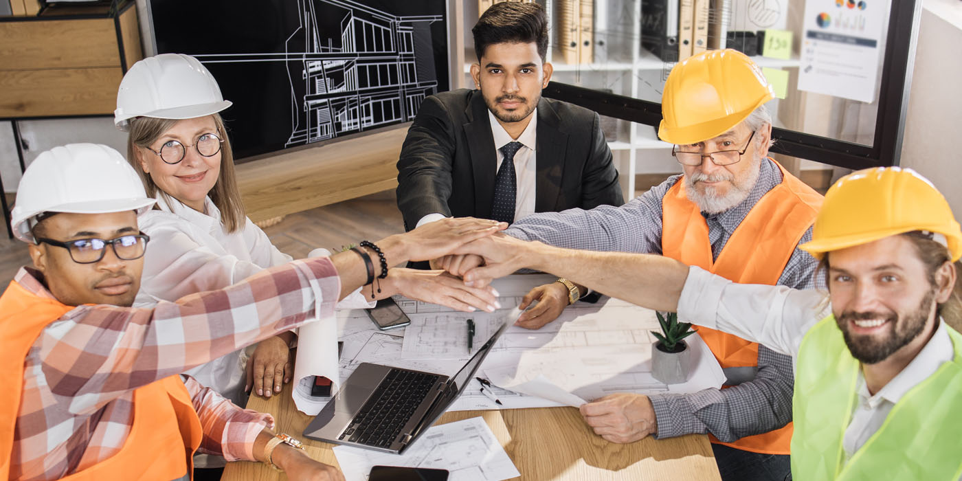Group of contractors and subcontractors sitting at a desk and putting their hands on each others hands as a symbol or collaboration